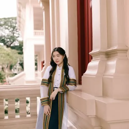 บัณฑิตสวมสายสะพายยืนข้างเสาตึกเก่า